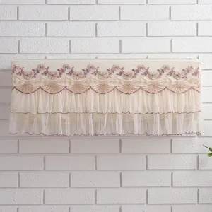 Close-up detail of beige lace hanging air conditioner dust cover with elegant floral embroidery.