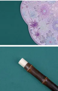 Nahaufnahme eines traditionellen chinesischen Fächers mit Stickerei, lila Stoff und Bambusgriff.