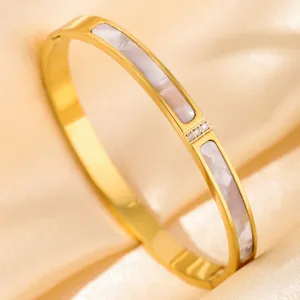 Detailed close-up of golden stainless steel bangle bracelet featuring white inlay and cubic zirconia.