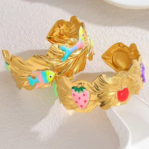 Scatto dettagliato di ampi bracciali rigidi dorati con ciondoli smaltati a forma di pesce e fragola.