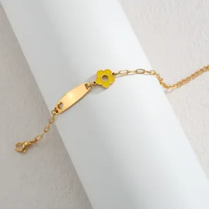 Nahaufnahme Detail des goldfarbenen Edelstahl Armbands mit gelber Blume und blankem Schild.