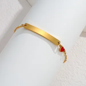 Detailansicht des goldenen Edelstahl-Armbands mit gravierbarer Platte und rotem Herz-Anhänger.