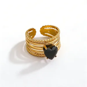 Close-up detail of a gold-plated multi-band stackable ring featuring a striking black heart stone.
