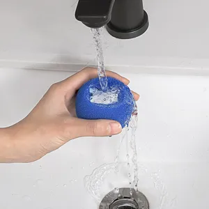 Primo piano della sfera in spugna per pulizia risciacquata sotto l'acqua corrente.