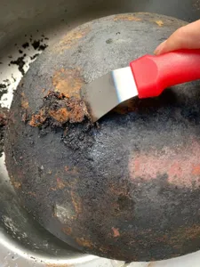 Gros plan détaillé d'un grattoir de casserole nettoyant la suie et la crasse brûlée.