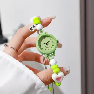 Detalle de un reloj de cuarzo para mujer con correa de cuentas verdes y colgante de corazón.