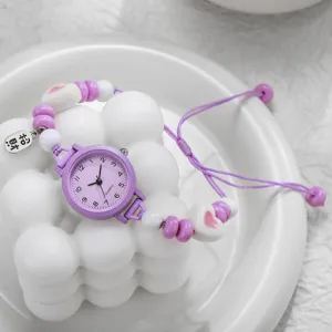Vista macro de un reloj de cuarzo morado con correa tejida de cuentas y dijes de corazón