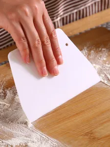 Gros plan d'une raclette à pâte en plastique blanc sur une planche en bois avec de la farine.