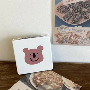 Close-up detail of white portable folding makeup mirror with cute pink bear face on wooden desk.