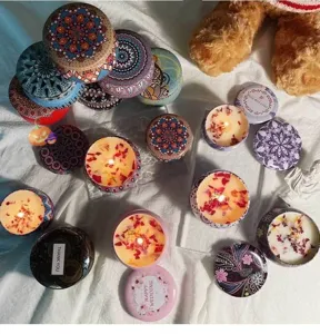 Vue détaillée de bougies parfumées en boîtes métalliques à motifs avec des fleurs séchées.