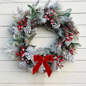 Detailansicht des schneebedeckten Weihnachtskranzes mit Zapfen, roten Beeren und Samtschleife.