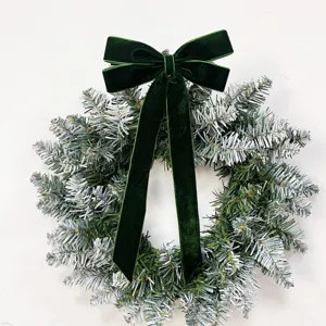 Detailed close-up of dark green velvet Christmas bow attached to frosted pine wreath for festive decor.