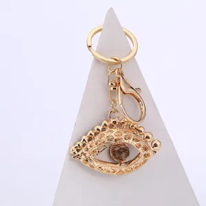 Gold metal evil eye keychain detail shot, elegant demonic eye hanging accessory charm.