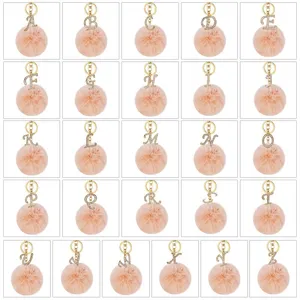 Detail view of rhinestone alphabet letter metal keychain with fluffy pink pom pom charms.