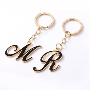 Close-up detail of gold metal keychain with black enamel letter pendant, stylish accessory.