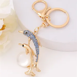 Gold dolphin keychain with blue rhinestones and pearl pendant, elegant metal bag charm detail.