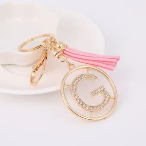 Close up of gold metal rhinestone letter G keychain pendant with pink tassel detail display.