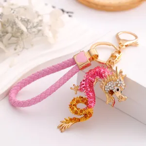 Close-up detail of the pink and gold rhinestone dragon keychain pendant with braided leather strap.