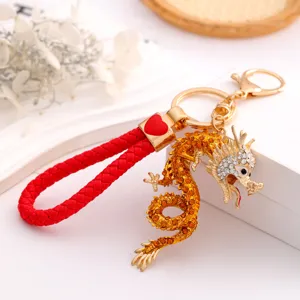 Close-up detail of the golden rhinestone dragon keyring, featuring a red woven leather strap.