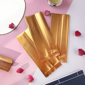 Draufsicht auf drei mattgoldene Aluminium-Teeverpackungsbeutel auf rosa Hintergrund