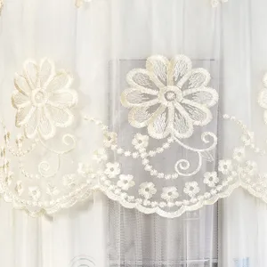 Close-up detail of white sheer mesh fabric with elegant beige floral embroidery and scalloped hem.