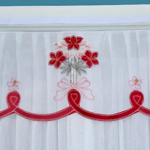 Close-up detail of white sheer door curtain with red floral embroidery and bow design.