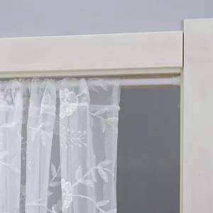 Λεπτομέρεια λευκής δαντελωτής κουρτίνας πόρτας με λουλουδάτο κέντημα και λευκή τηλεσκοπική ράβδο.