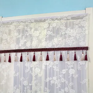 Detail shot of white lace curtain with elegant wine red tassel trim and textured decorative ribbon.