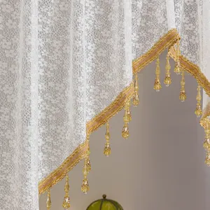 Λεπτομερης οψη κομψης λευκης δαντελωτης κουρτινας με χρυσο τελειωμα και κρεμαστα χαντρωτα κρόσσια.
