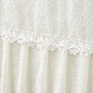 Close-up detail of white plush fabric with delicate floral lace trim and faux pearl accents.