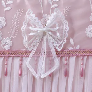Dettaglio copertura antipolvere TV in pizzo rosa con ricamo floreale e fiocco.
