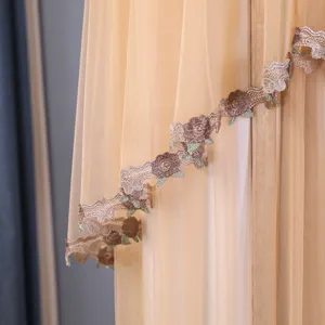 Dettaglio copri condizionatore rotondo verticale, tessuto a rete beige con bordo in pizzo marrone.