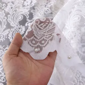 Weißes Spitzenstoff-Detail mit filigranem Blumenmuster und Perlendekor für den Wohnbereich.