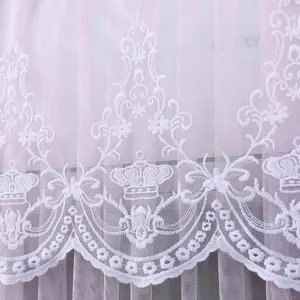 Primo piano dettagliato del ricamo in pizzo bianco con corona su tessuto in tulle.