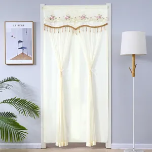 Rideau de porte en dentelle beige avec broderie florale et cantonnière à pompons.