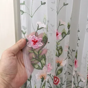 Close-up of white sheer curtain with delicate pink floral embroidery and translucent texture.