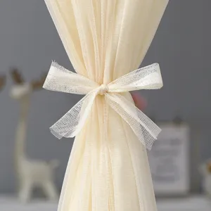 Close-up detail of beige sheer mesh curtain with elegant bow tieback decoration.