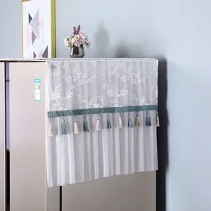 Detailed view of a white lace refrigerator dust cover with elegant tassels and green trim.