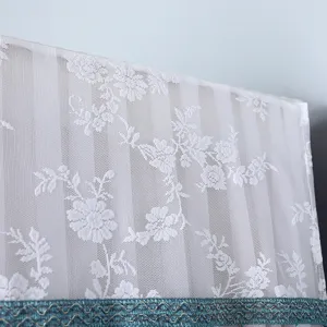 Closeup detail of white lace dust cover showing exquisite floral embroidery texture and trim.