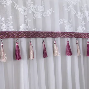 Close-up of white lace fabric detail with purple embroidered trim and hanging tassels.