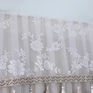 Detailed view of white lace dust cover with floral embroidery and decorative beaded fringe trim.