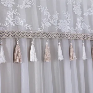 White lace dust cover detail featuring elegant floral embroidery, ribbon and hanging tassels.