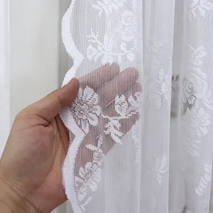 Detailopname van wit kantgordijn, met weefselstructuur en doorschijnend bloemenpatroon.