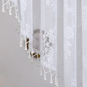 Gedetailleerde close-up van wit kantgordijn met elegante parelhangerhangers en gebogen rand.