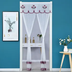 Detailed view of white sheer door curtain with purple floral embroidery and bottom bands in room.