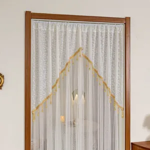 Close-up view of the elegant white lace door curtain with golden beaded fringe trim in room.