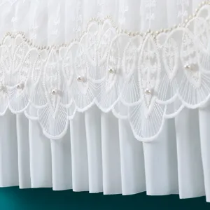 Primo piano della copertura antipolvere ricamata in pizzo bianco con perle e pieghe delicate.