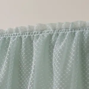 Gros plan de tissu en tulle dentelle vert clair avec bord volanté et motif à pois.