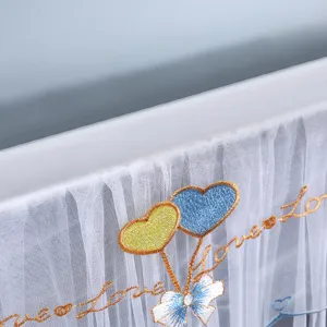 Dettaglio in primo piano della copertura antipolvere TV in pizzo bianco con cuori e fiocchi ricamati.