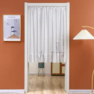 Close-up detail of white lace door curtain hanging in room, showing delicate floral pattern.